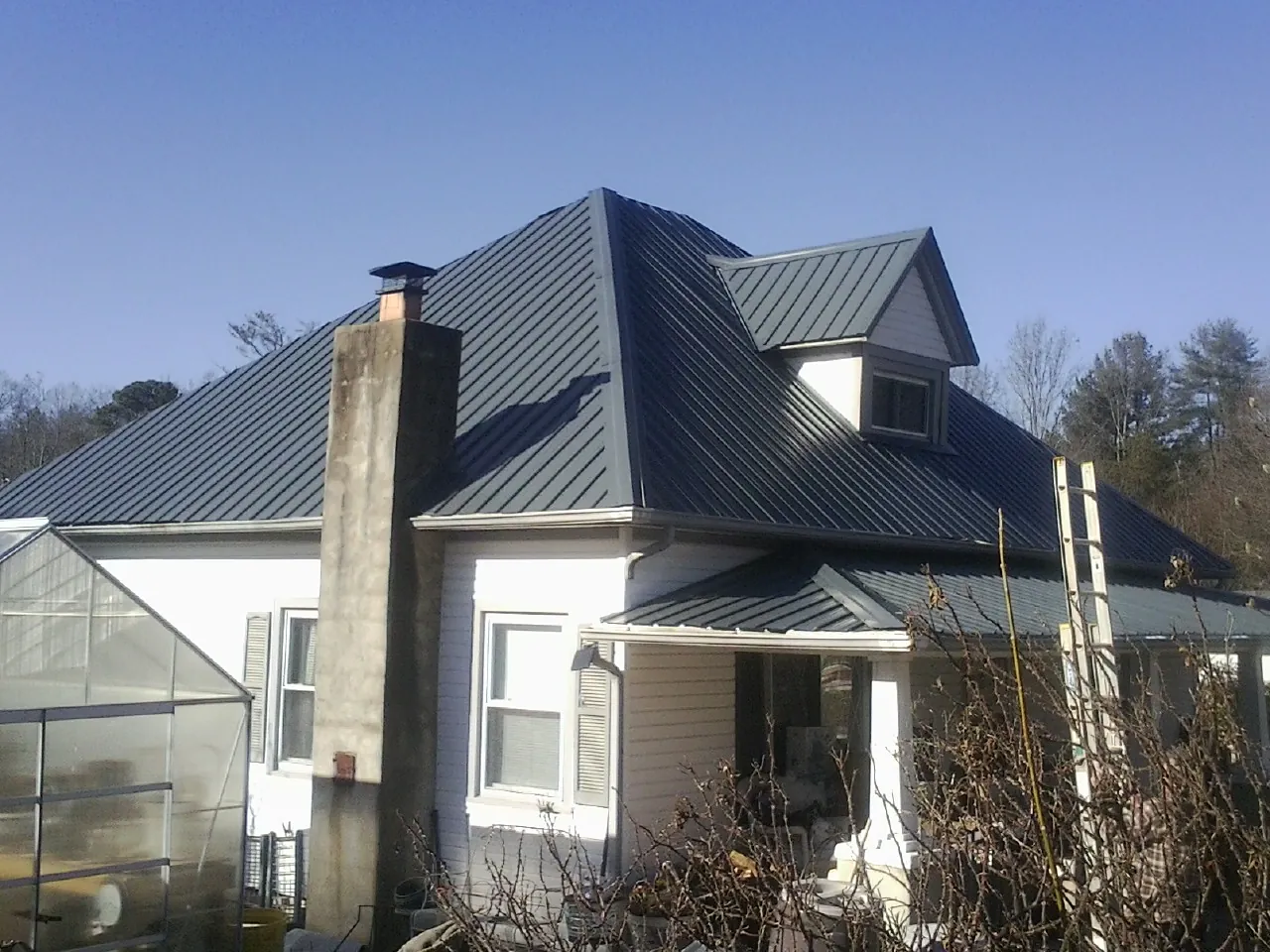 Dark blue standing seam metal roof on a white farmhouse with dormer in Bethel